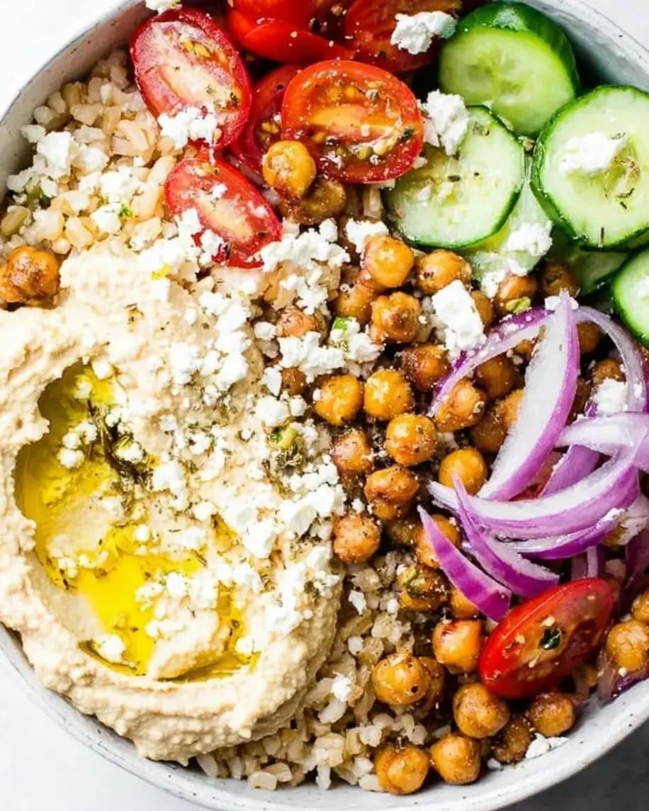 A vibrant Mediterranean Hummus Bowl with fresh vegetables, olives, feta, and a drizzle of olive oil.